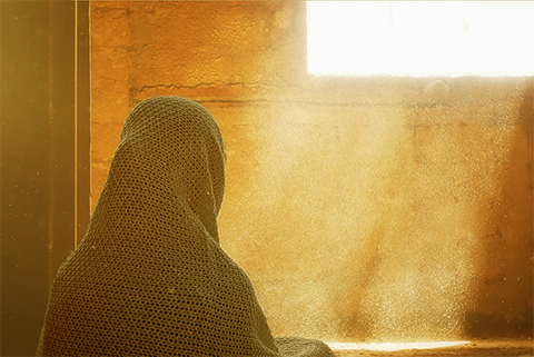 mujer con la cabeza cubierta observa como entra la luz por la ventana